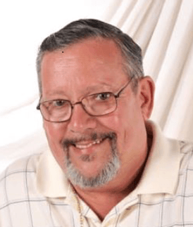 Smiling middle-aged man with glasses and a goatee wearing a white grid-patterned polo shirt.